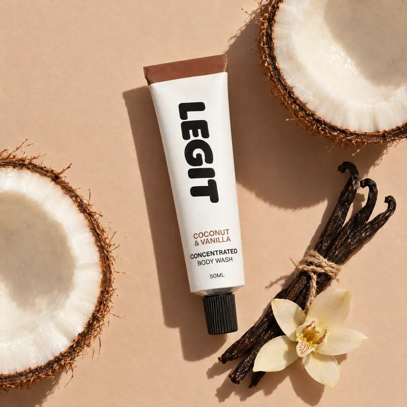 A tube of Legit Coconut & Vanilla between two halved coconuts, with vanilla pods and a vanilla orchid
